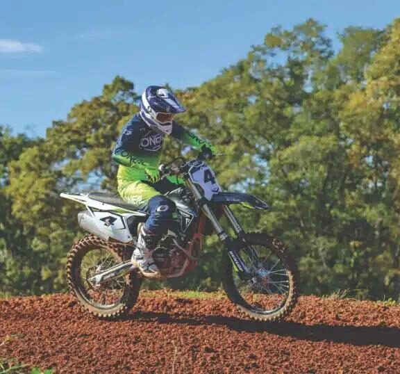 Rider en tenue O'Neal vert fluo en action sur un terrain de motocross en terre rouge