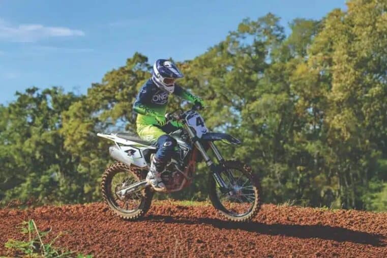 Rider en tenue O'Neal vert fluo en action sur un terrain de motocross en terre rouge