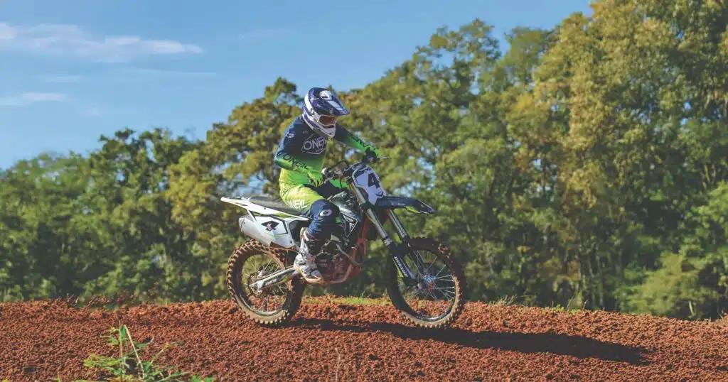 Rider en tenue O'Neal vert fluo en action sur un terrain de motocross en terre rouge