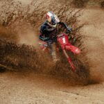 Pilote de motocross en virage dans une gerbe de terre, masque 100% Ultra Hydro